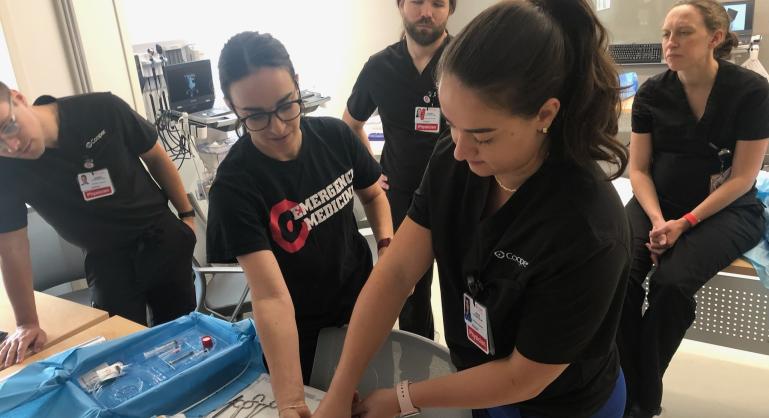 Medical residents in a simulation lab practicing a hands-on procedure on a training model under faculty supervision.