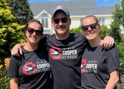 A trio of individuals stand closely together wearing Cooper Emergency Medicine tee shirts.