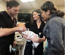 Medical team examining a newborn in a clinical setting, with one provider using a stethoscope.